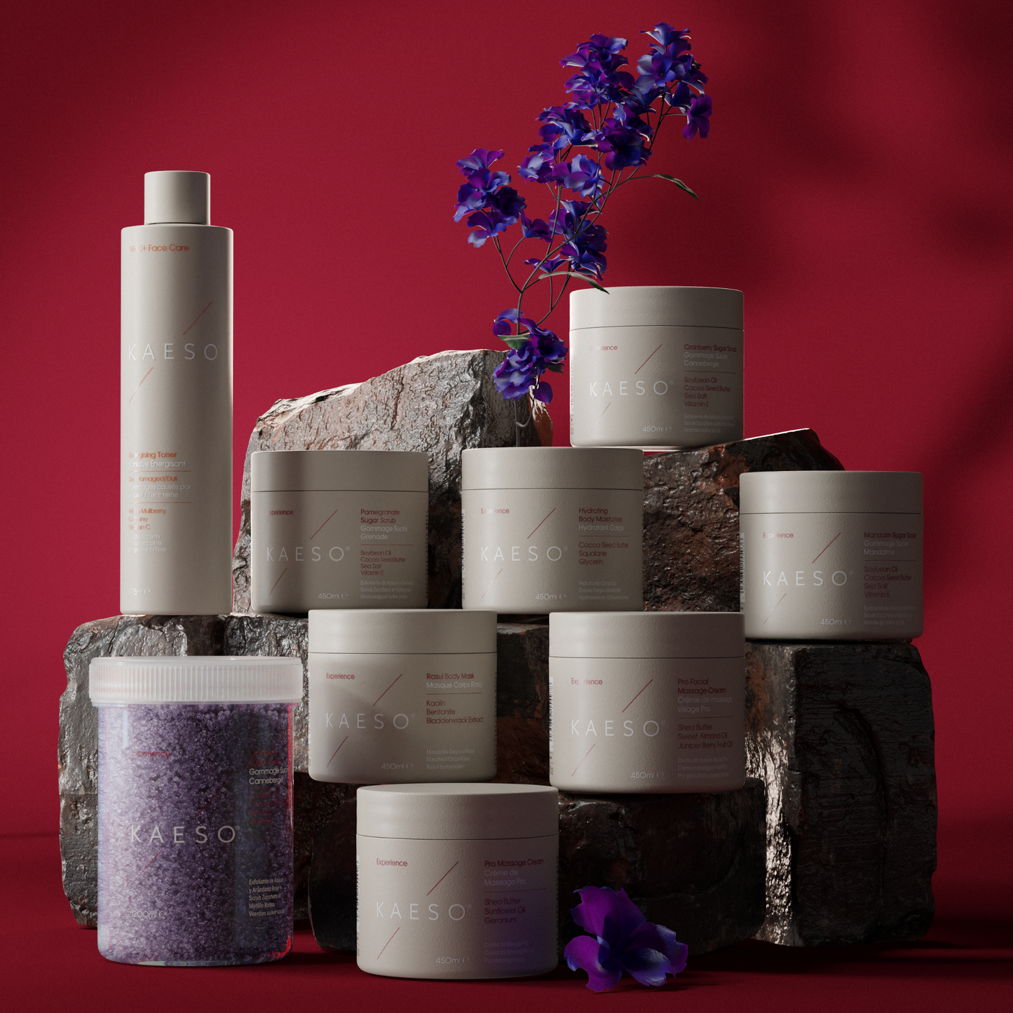 A collection of KASEO skincare products in matte off-white packaging, including a tall bottle and multiple jars, styled on dark textured stone blocks against a deep red background with purple flowers