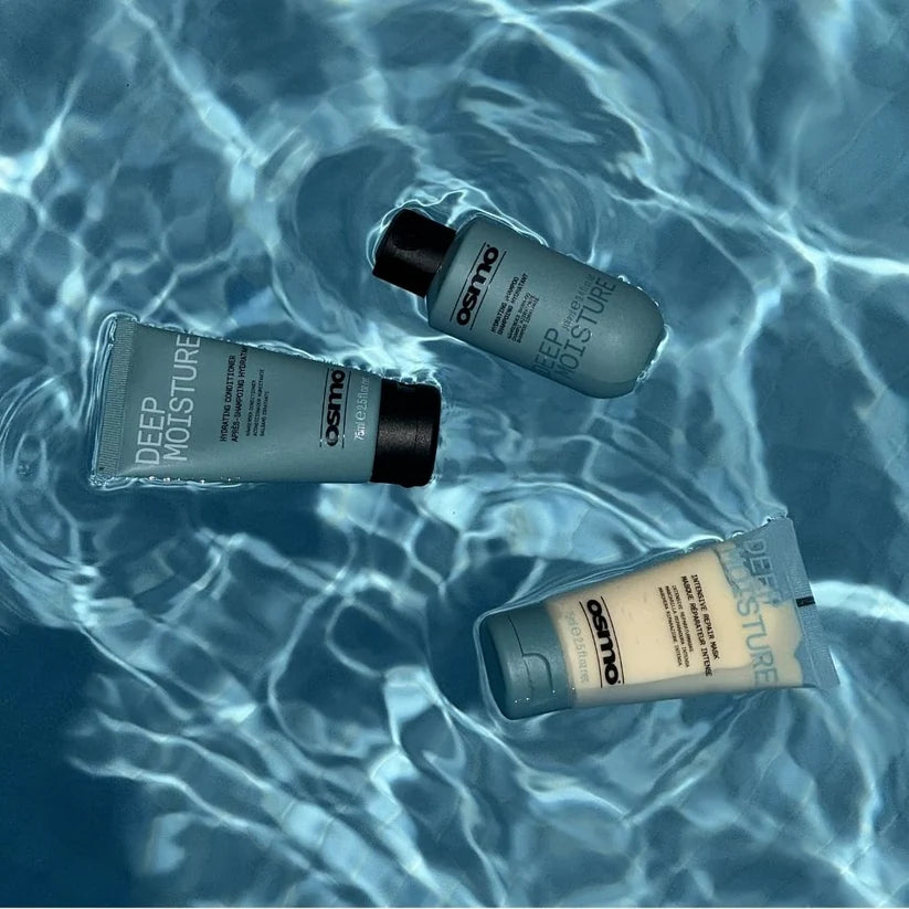 Three Oettmo Deep Moisture skincare tubes floating on rippling blue water. Two are light gray with black caps, and one is a warm beige tube with a gray cap.