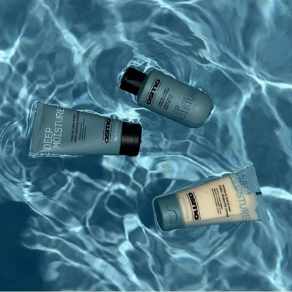 Three Oettmo Deep Moisture skincare tubes floating on rippling blue water. Two are light gray with black caps, and one is a warm beige tube with a gray cap.