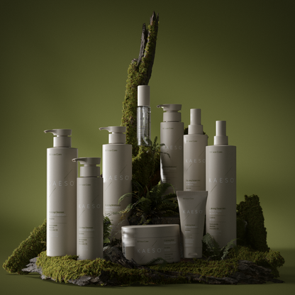 A collection of white and clear skincare bottles and tubes from the brand CAESAO, styled on a mossy base with a tree trunk prop against a dark olive green background.