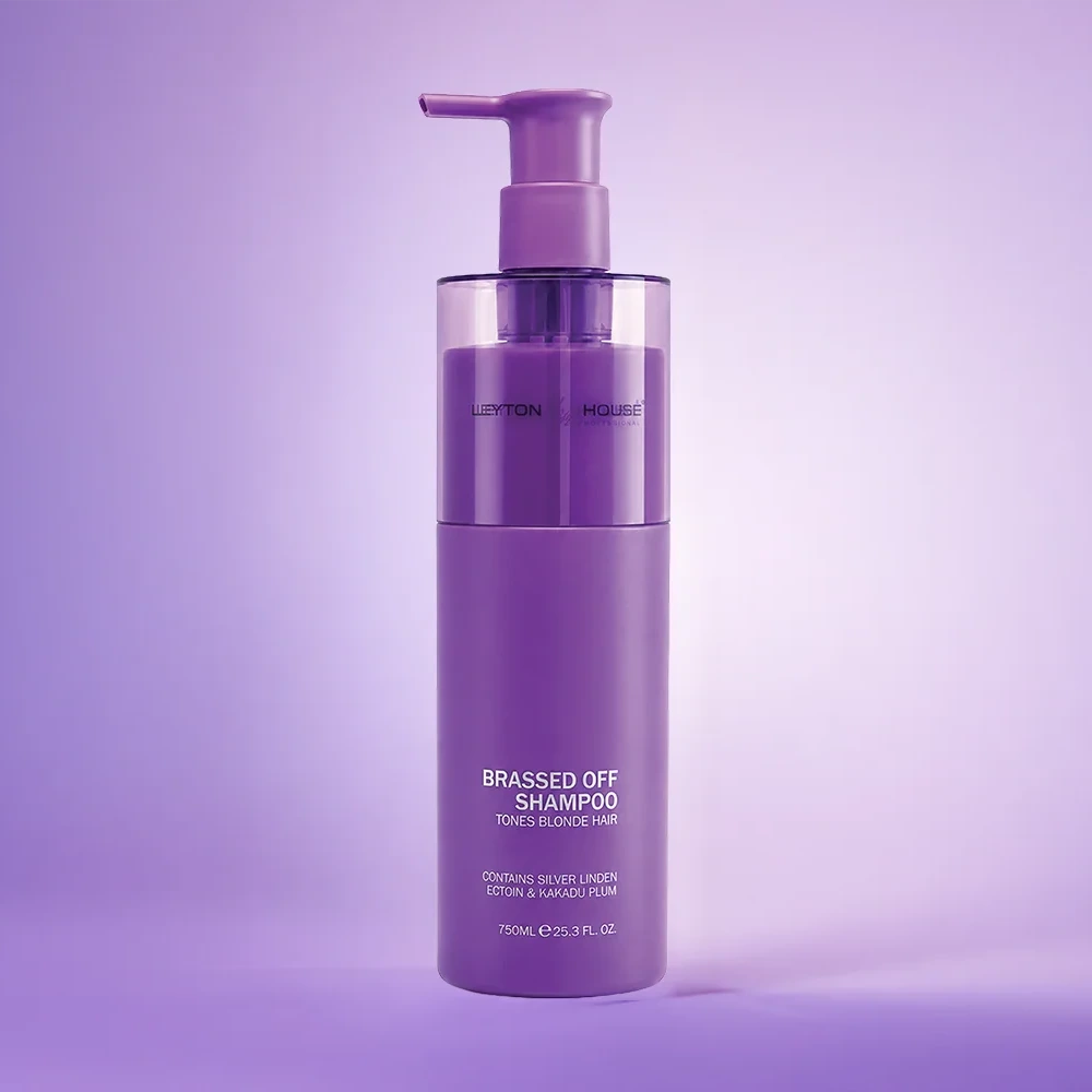 A bottle of Lofton Haircare Brassed Off Shampoo in a solid purple color, featuring a matching purple pump dispenser, set against a matching purple gradient background.