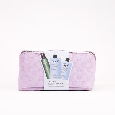 A lavender and white checkered cosmetic pouch with a zipper closure, featuring a white paper insert in front displaying two skincare bottles from REF. The pouch is photographed on a clean white background.