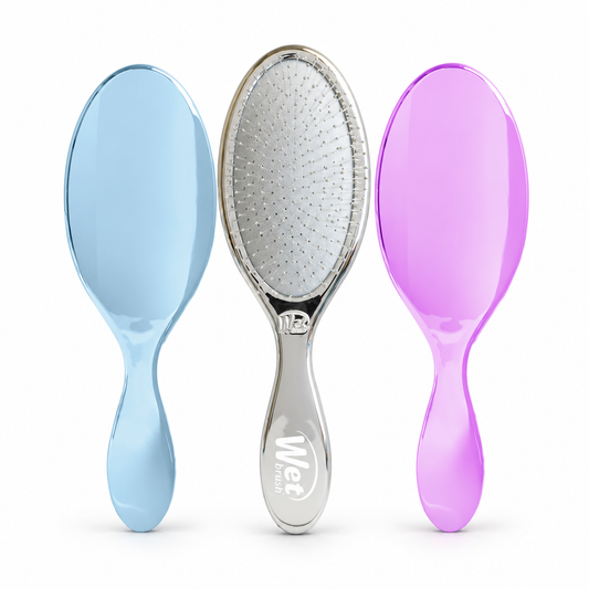 Three oval-shaped hairbrushes with glossy handles are shown side by side on a white background. The left brush has a light blue handle, the center brush has a silver handle with a white bristle head, and the right brush has a purple handle.