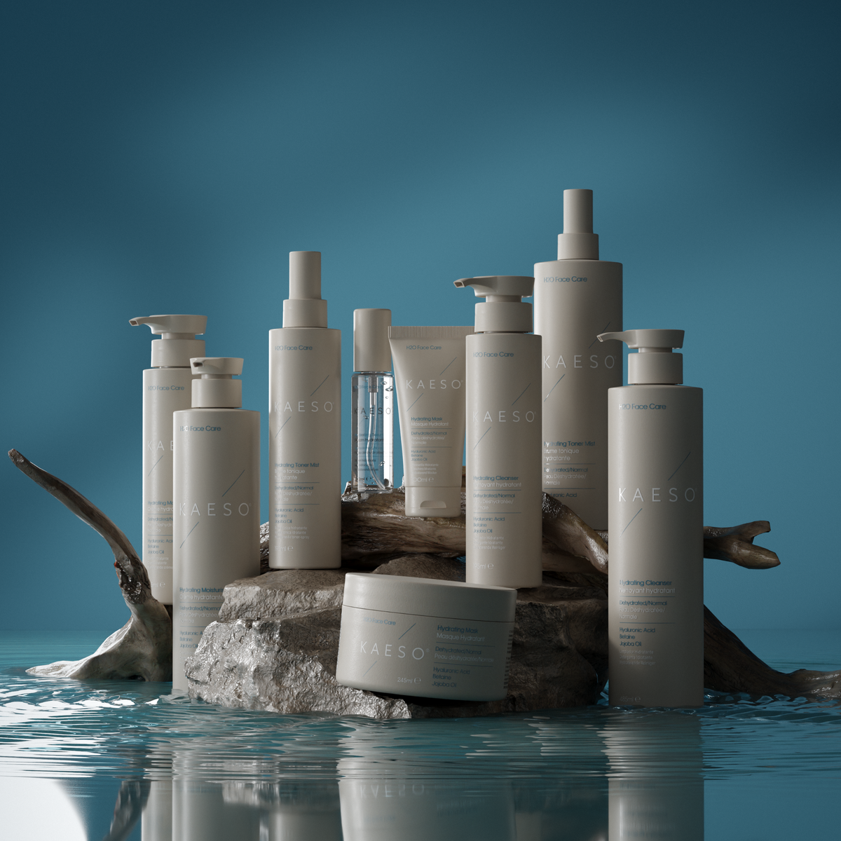 A collection of KAESO skincare and haircare products in matte white and clear packaging, styled on a piece of driftwood over still water against a deep blue gradient background.