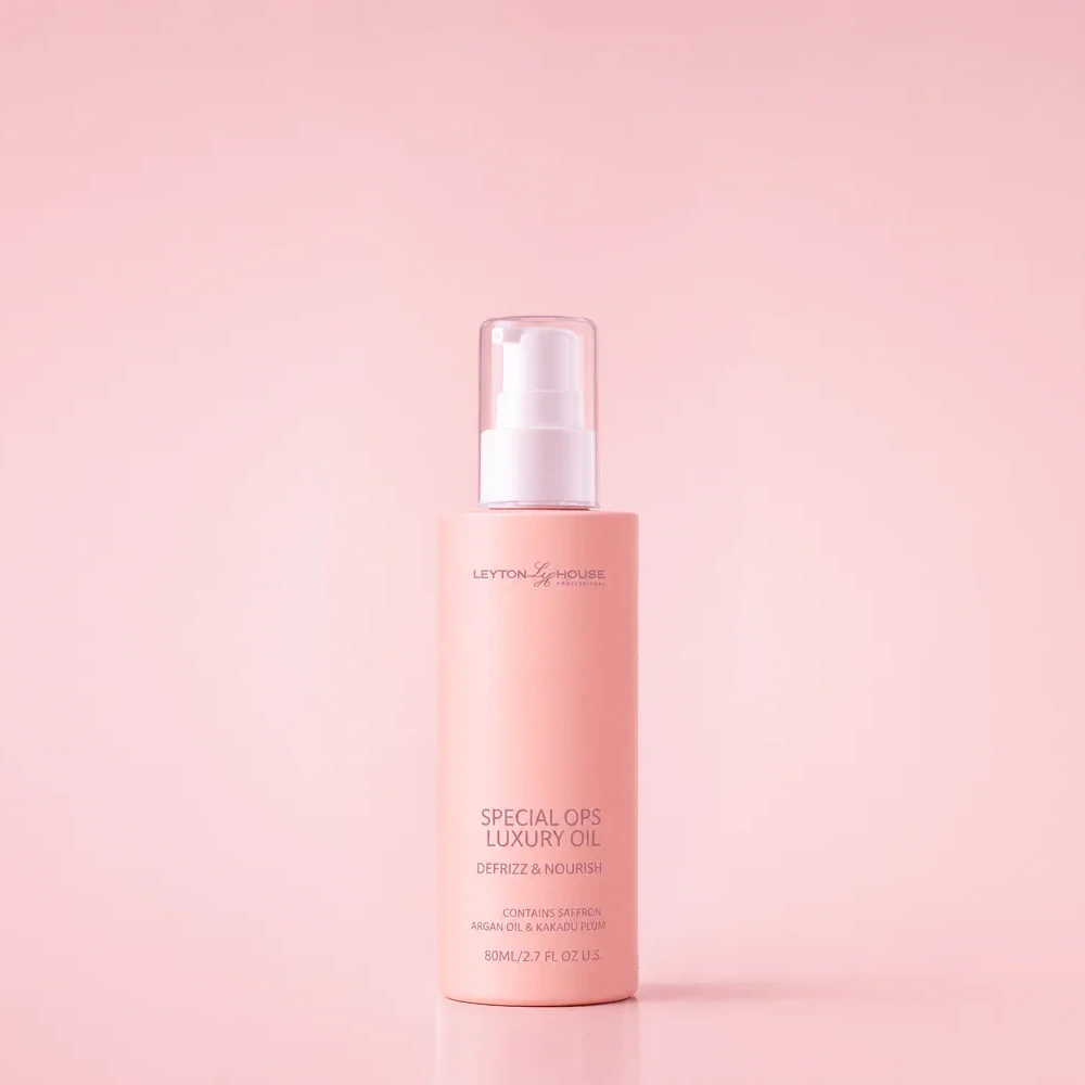A bottle of Layton Cosmetics Special Ops Luxury Oil with a light pink body and a white pump dispenser, set against a solid light pink background.