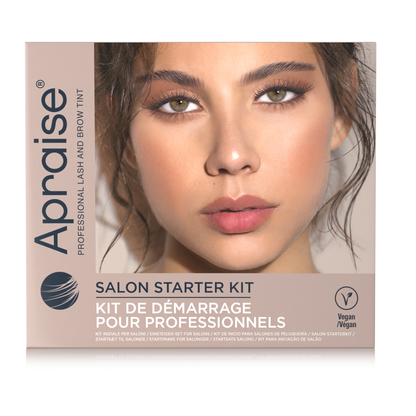 A rectangular box for the Apraise Salon Starter Kit, featuring a close-up photo of a woman's face with defined eyebrows and nude pink lips. The box is beige and white with black and blue text, and includes a 'Vegan' logo on the bottom right.