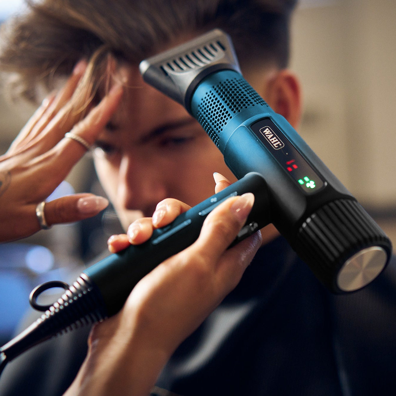 Person using a hair dryer on another person's head with a blurred background