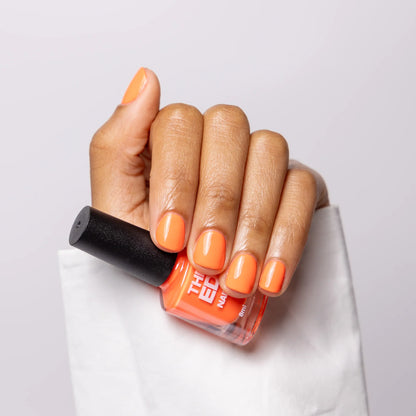 Hand with orange nail polish holding a bottle of orange nail polish.