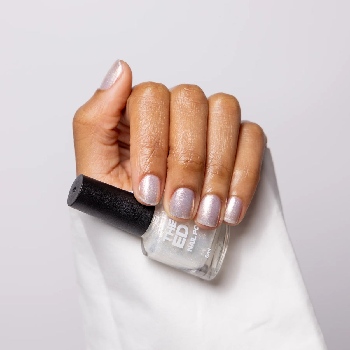 Hand holding a bottle of nail polish with a light gray background