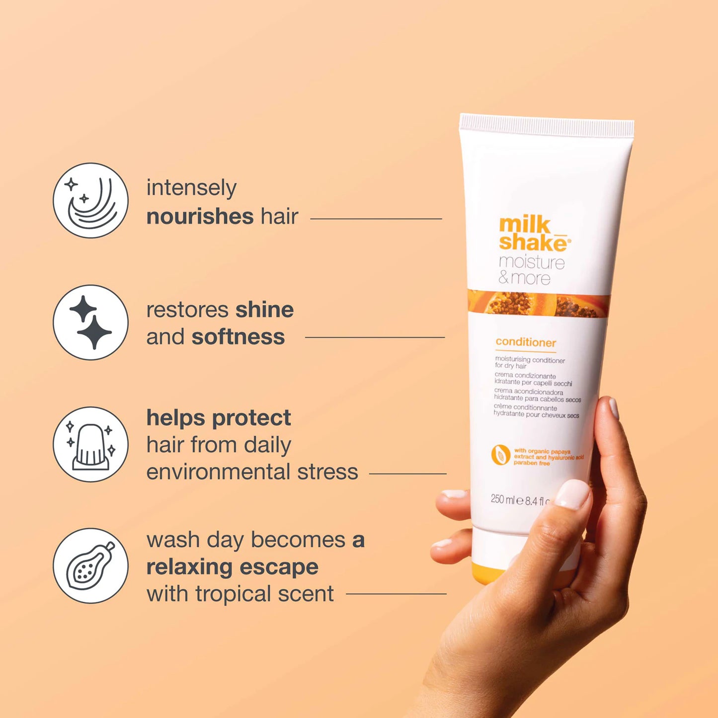 Hand holding a tube of milk_shake conditioner with product benefits on a beige background
