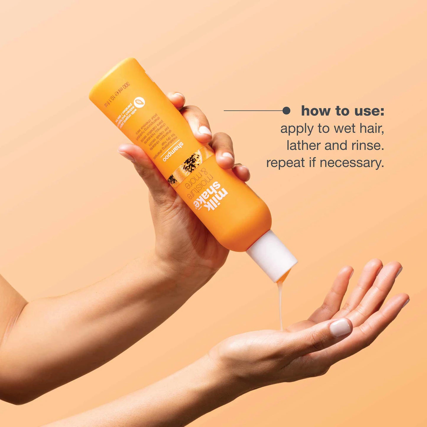 Orange bottle of shampoo held by a hand with product being dispensed onto another palm against a beige background.