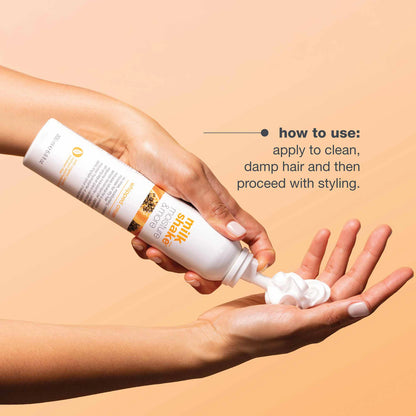 Hand holding a bottle of hair care product with text on how to use it against a beige background