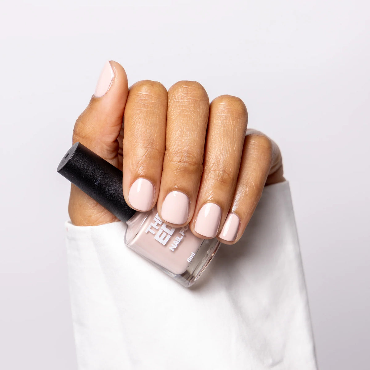 Hand holding a bottle of nail polish with light pink nails on a white background