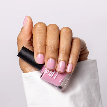 A hand holding a bottle of nail polish with light pink nails painted, against a clean white background. 